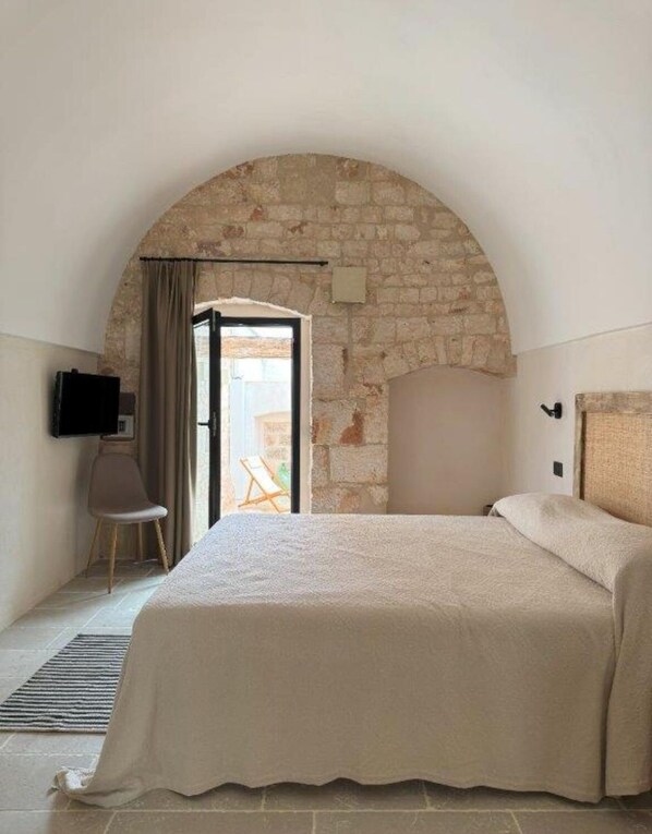 Ein Schlafzimmer mit steinbogiger Nische, einem Bett, einem Sessel und einem Fernseher.