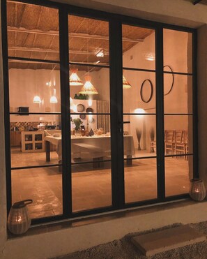 Enjoy meals in this spacious room with a large glass door leading to a dining area, featuring a high ceiling and pendant lights.