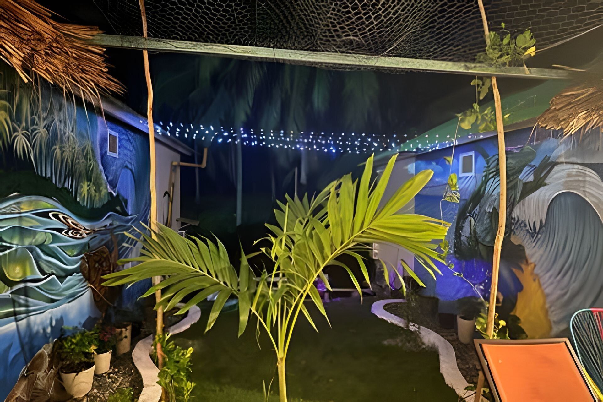 Una habitación con un mural de paisaje tropical, un pequeño jardín interior y una estructura con techo de paja.