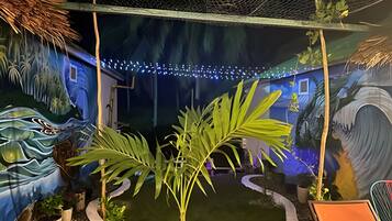 Una habitación con un mural de paisaje tropical, un pequeño jardín interior y una estructura con techo de paja.