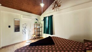 A bedroom with a bed, a fan, a shelf with towels, a wall decoration, and a ceiling fan.