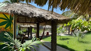 A thatched-roof structure with a patio area, surrounded by lush greenery and a well-maintained lawn.