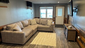 A living room with a sectional sofa, a rug, a wooden cabinet, and a door with a window. - "Ackerman Lakeside" - 3 Story, 4 Bed, 3 Bath (South Minnewaukan)