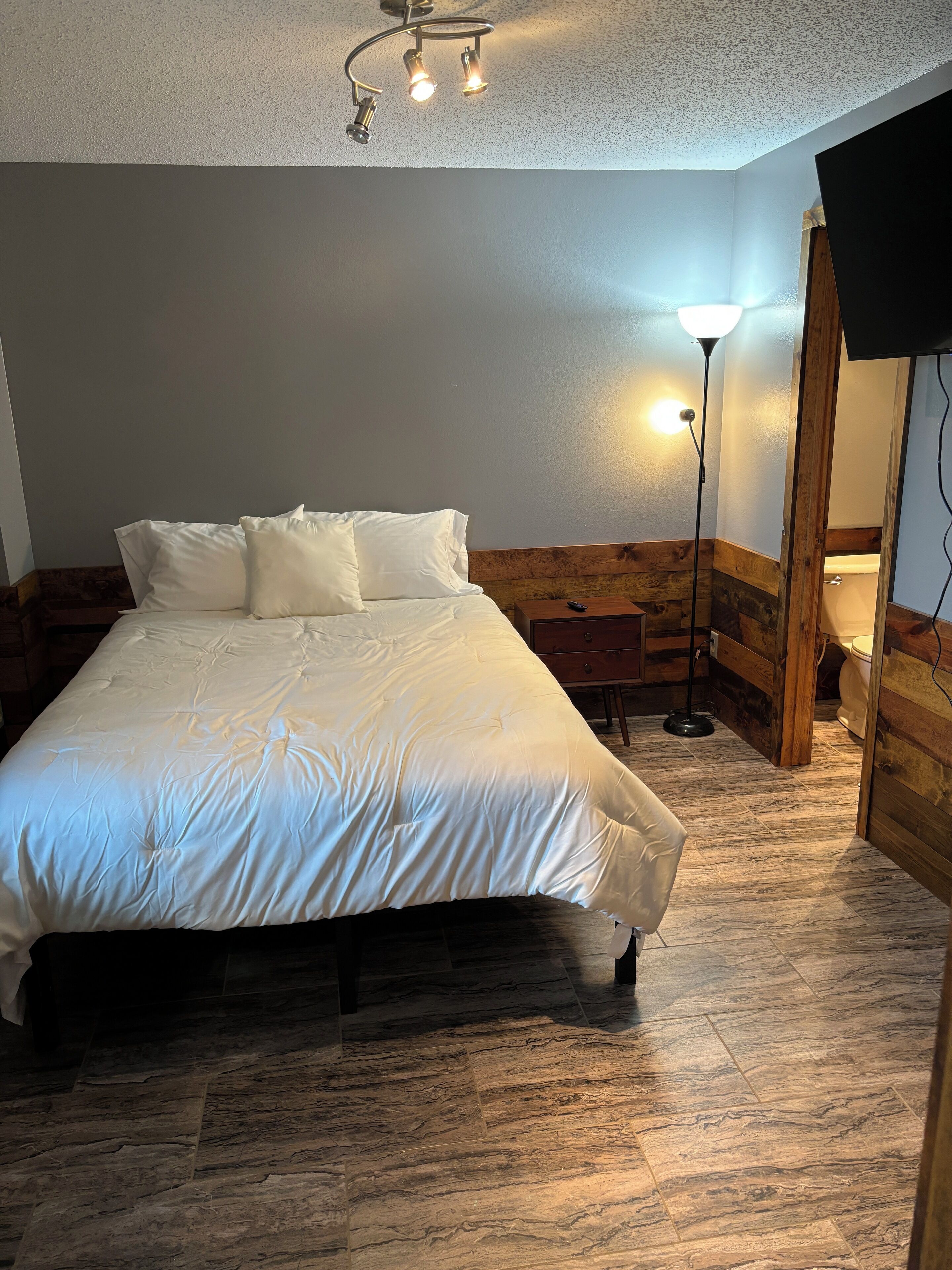 Un dormitorio con una cama grande, un cabecero de madera, una mesita de noche, una lámpara de pie y un panel de pared de madera.