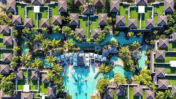 Vue aérienne d’un complexe hôtelier comprenant plusieurs hébergements de type bungalow, une piscine centrale et une végétation luxuriante.
