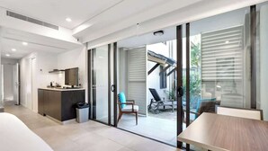 Une chambre d’hôtel moderne dotée d’un coin cuisine, d’une table à manger et d’une porte-fenêtre coulissante donnant sur un espace extérieur aménagé.