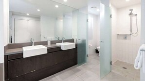 Une salle de bain moderne avec un meuble-lavabo en bois foncé, deux vasques, un grand miroir et une cabine de douche en verre.