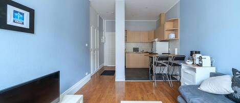 A compact living space with a sofa, a TV, a kitchen area, and a dining table.