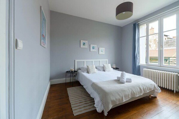 Un dormitorio con una cama grande, una mesita de noche pequeña, un radiador y una ventana con cortinas.