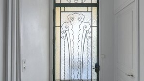 Passadís estret amb una porta que incorpora un panell de vidre decoratiu i una reixa de metall verd.