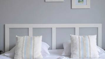 A neatly made bed with white linens and striped pillows, a rolled white towel, and three framed pictures on the wall above.