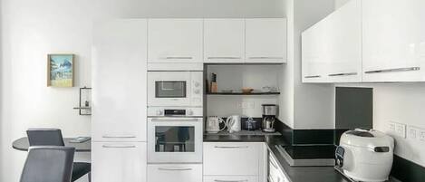 Une cuisine moderne avec des meubles blancs, un plan de travail noir, un four à micro-ondes, un four traditionnel, une machine à café et un lave-linge.