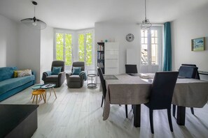 A modern living room with a blue sofa, two armchairs, a dining table with chairs, and a bookshelf. - Design apartment in the city center with parking (Vichy)