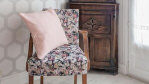 A chair with a floral pattern and a pink cushion, positioned in front of a wooden cabinet with glass doors.