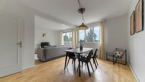 A modern living space with a dining area, a sofa, and a television. - Le Raymond - 48 allée des ailes - Vichy (Vichy)
