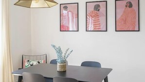A dining area with a table, chairs, a hanging lamp, and framed artwork on the wall. - Le Raymond - 48 allée des ailes - Vichy (Vichy)