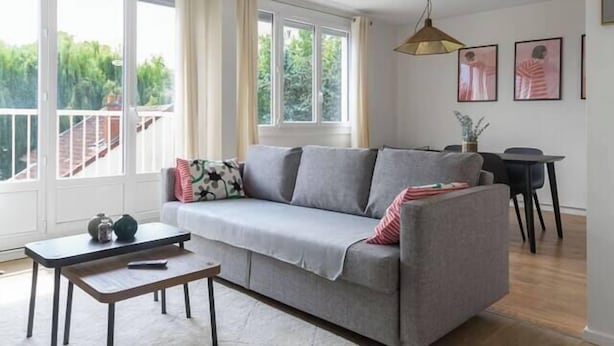 A modern living room with a grey sofa, a small table, and a dining area with a chair. - Le Raymond - 48 allée des ailes - Vichy (Vichy)