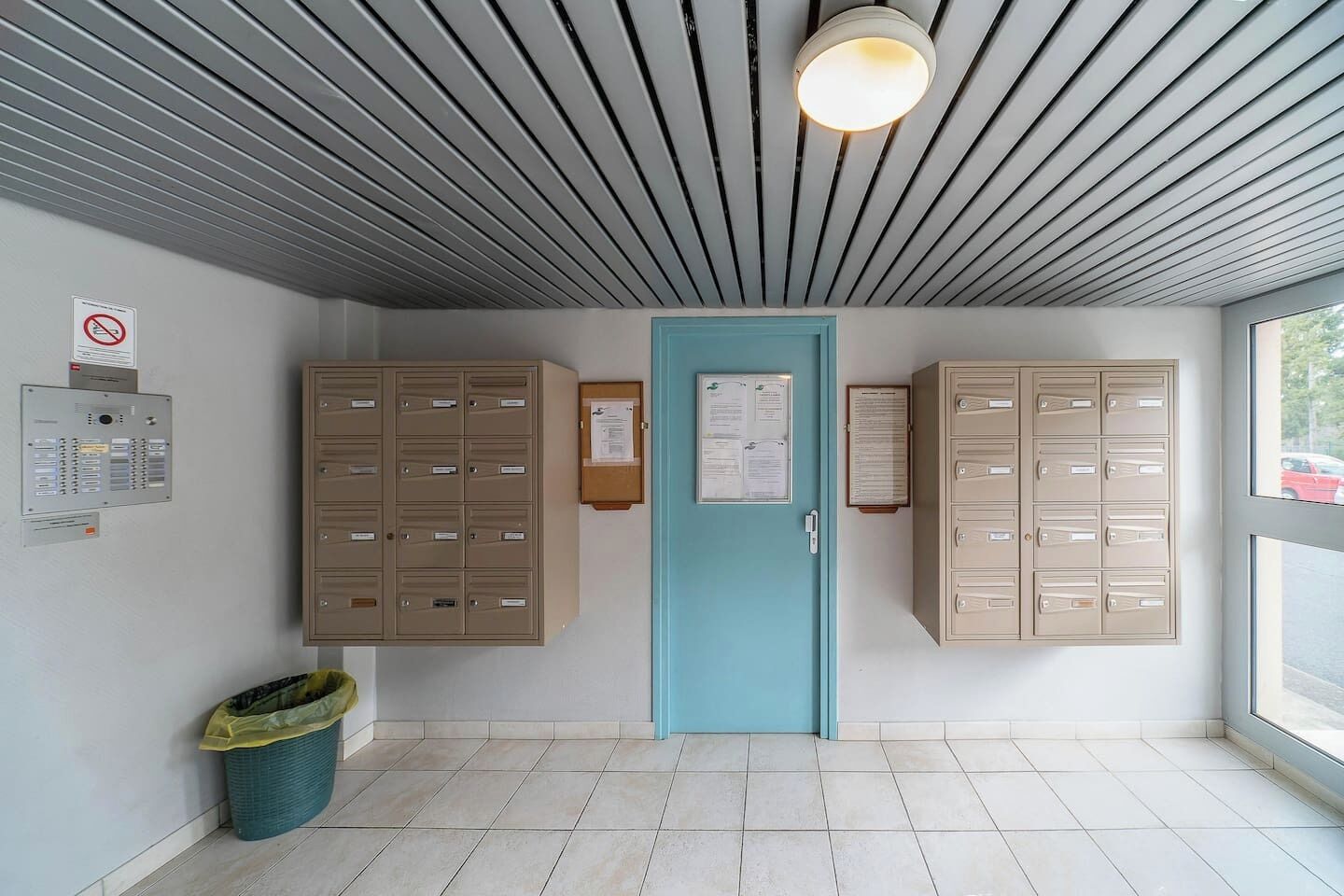 A room with a blue door, two beige filing cabinets, a trash bin, and a wall-mounted electrical panel.