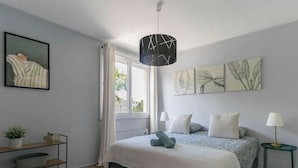 A bedroom with a bed, a window, a shelf, and a hanging light fixture. - Le Raymond - 48 allée des ailes - Vichy (Vichy)