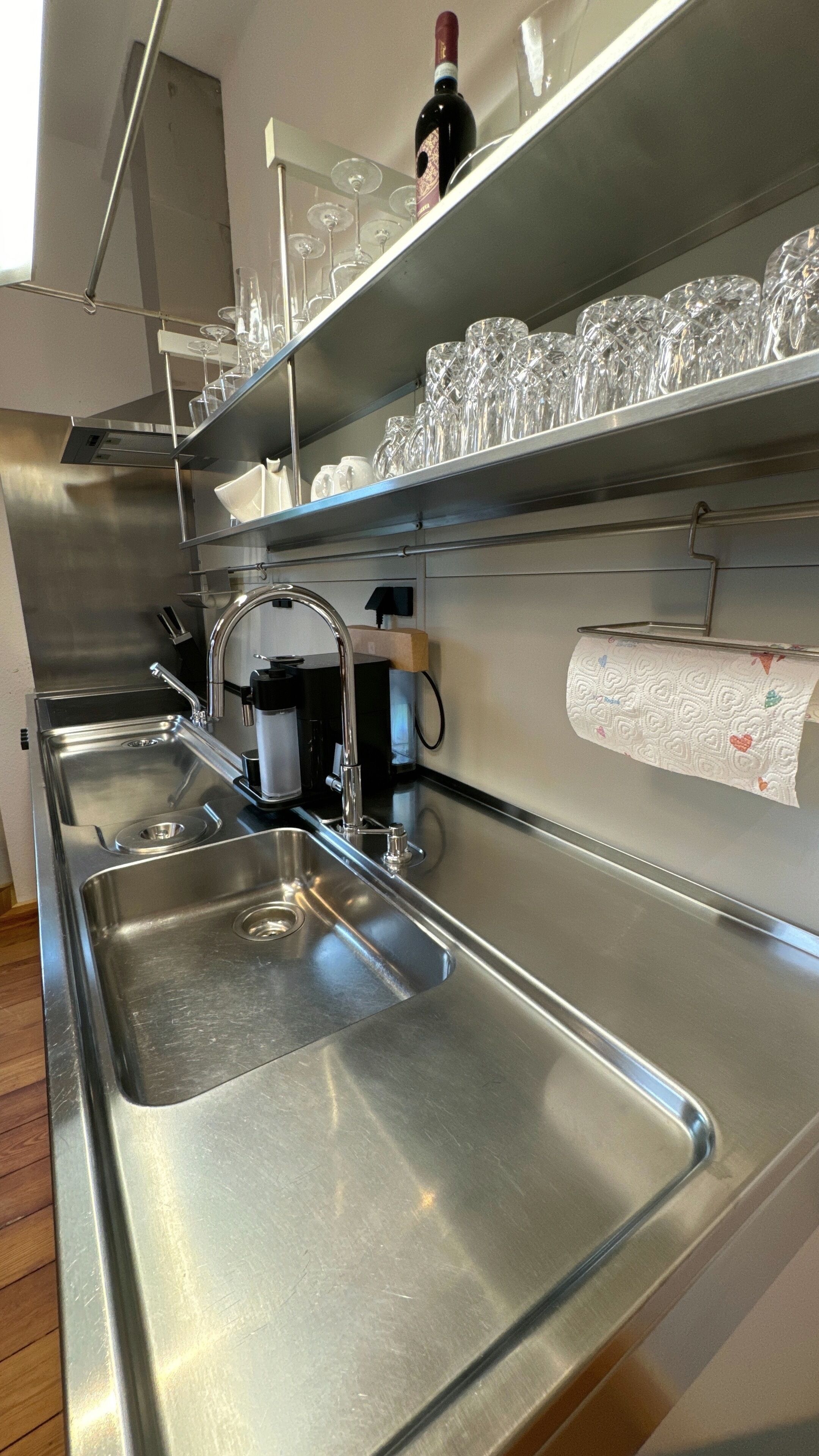 Une cuisine moderne dotée d’appareils électroménagers en acier inoxydable, une bouteille de vin posée sur l’étagère et un distributeur d’essuie-tout.