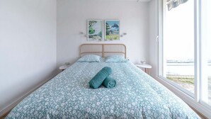 Un dormitorio con una cama, dos obras de arte en la pared, una ventana y vistas al exterior.