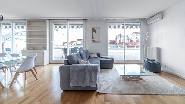Un amplio salón con un sofá gris, una mesa de comedor de cristal y un ventanal con vistas a la ciudad.