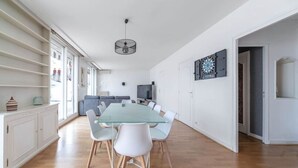 Un comedor amplio con una mesa de vidrio y sillas blancas, un televisor y un dardo en la pared.