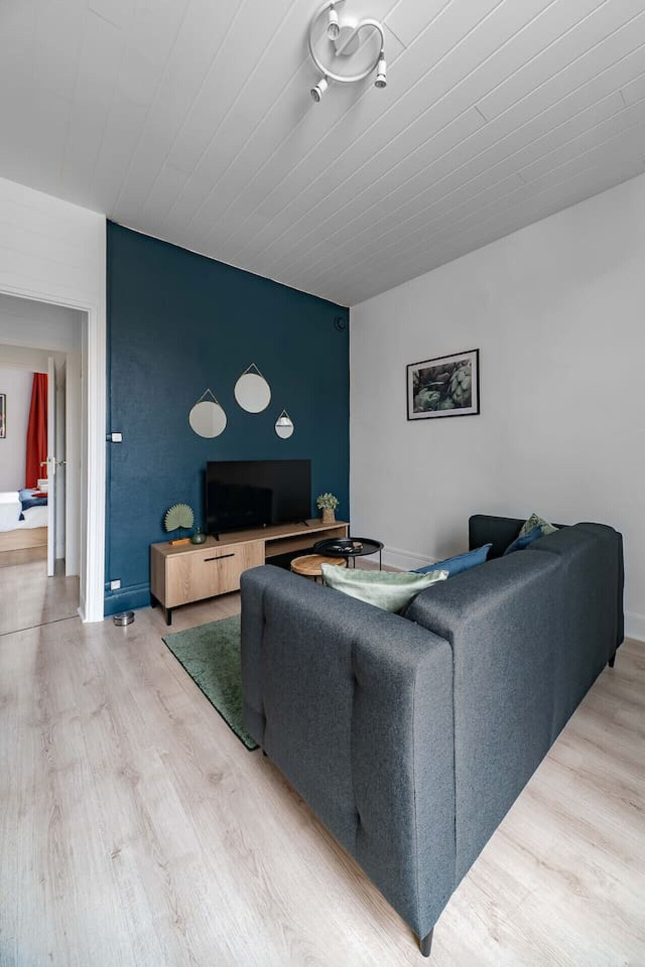 Een moderne woonkamer met een grijze bank, een tv-meubel van hout en een blauwe accentmuur.