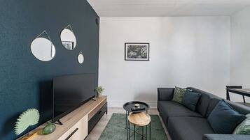 Ein modernes Wohnzimmer mit dunkler Akzentwand, einem Flachbildfernseher, einem dunklen Sofa und einem kleinen runden Couchtisch.