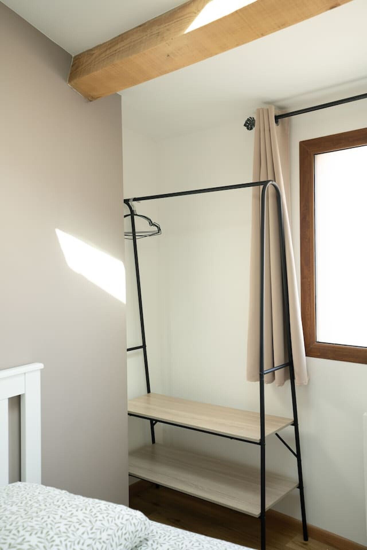 A bunk bed with a wooden ceiling beam, a window with curtains, and a radiator.