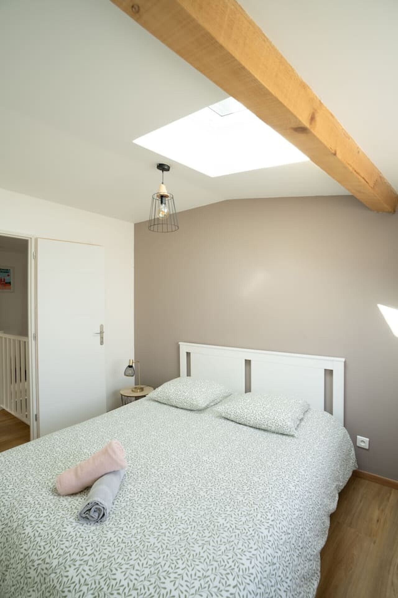 A bedroom with a sloped ceiling, a bed with a white headboard, and a skylight.