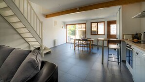 A spacious living area with a staircase, a dining table with chairs, and a kitchen area with a counter and appliances.