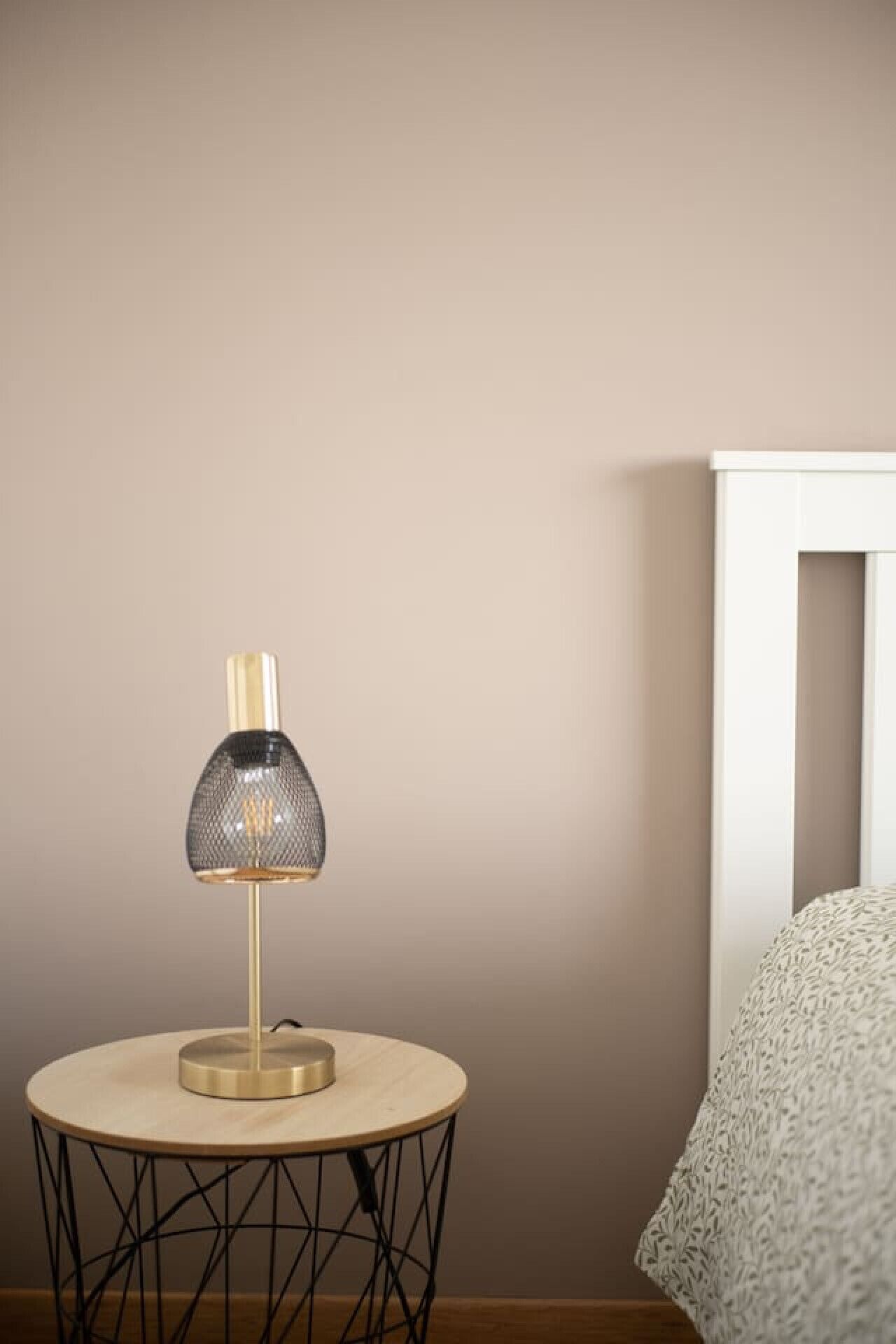 Un tavolo rotondo con una lampada e un letto addossato a una parete spoglia.