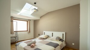 A bedroom with a bed, a skylight, a radiator, and a window with curtains.
