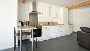 A modern kitchen with white cabinets, a stainless steel range hood, a dishwasher, and a dining area with a table and chairs.