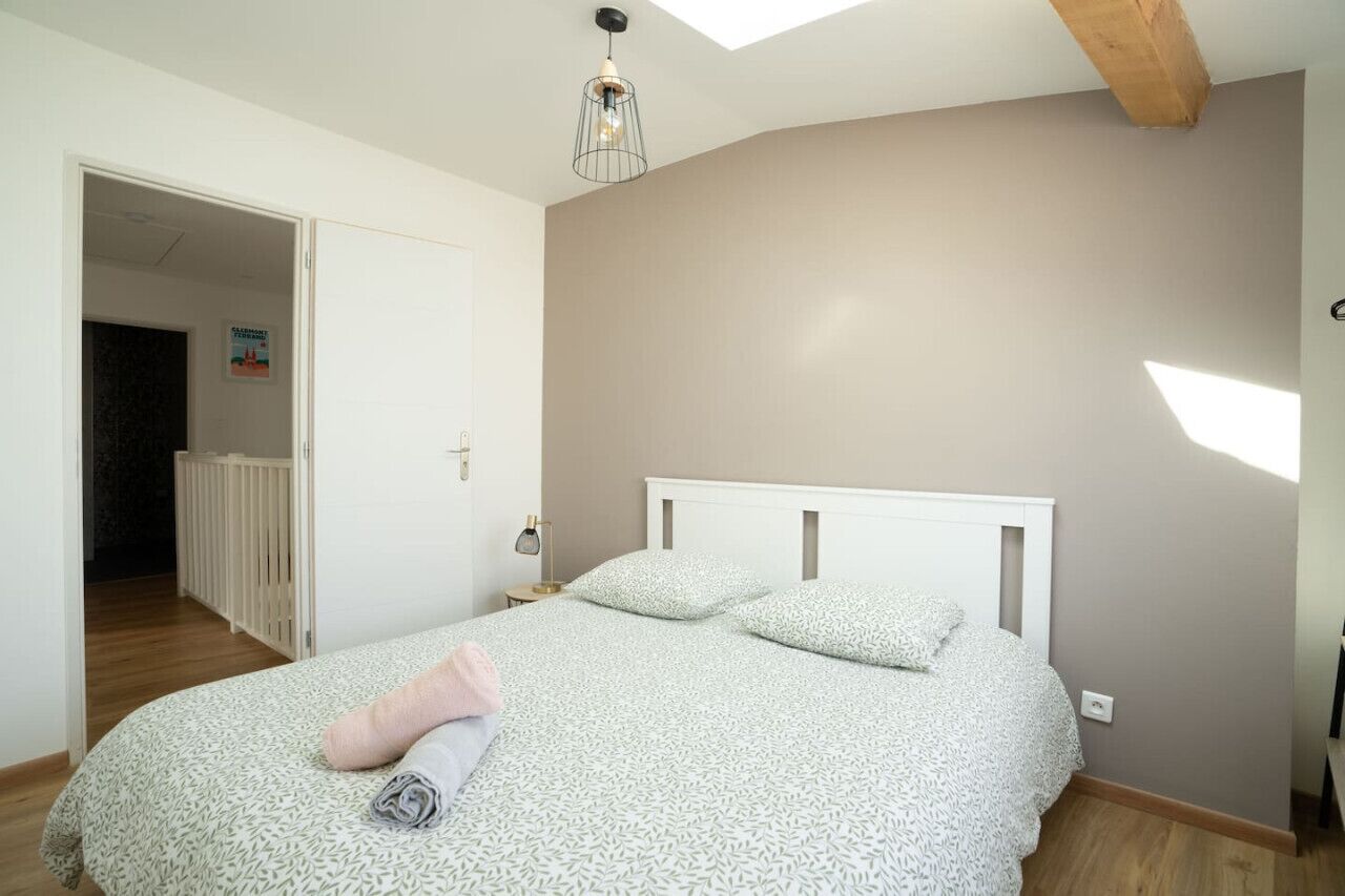 Un dormitorio con cama, lámpara de noche, lámpara colgante y una puerta que da a otra habitación.