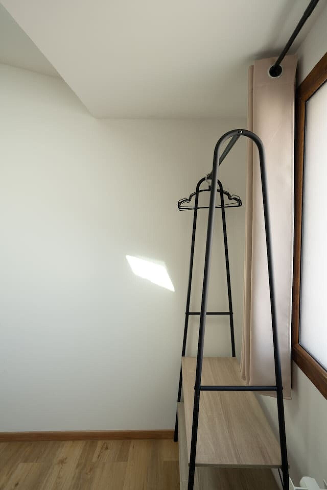 A room with a wooden floor, a black metal ladder, and a window with a white curtain.