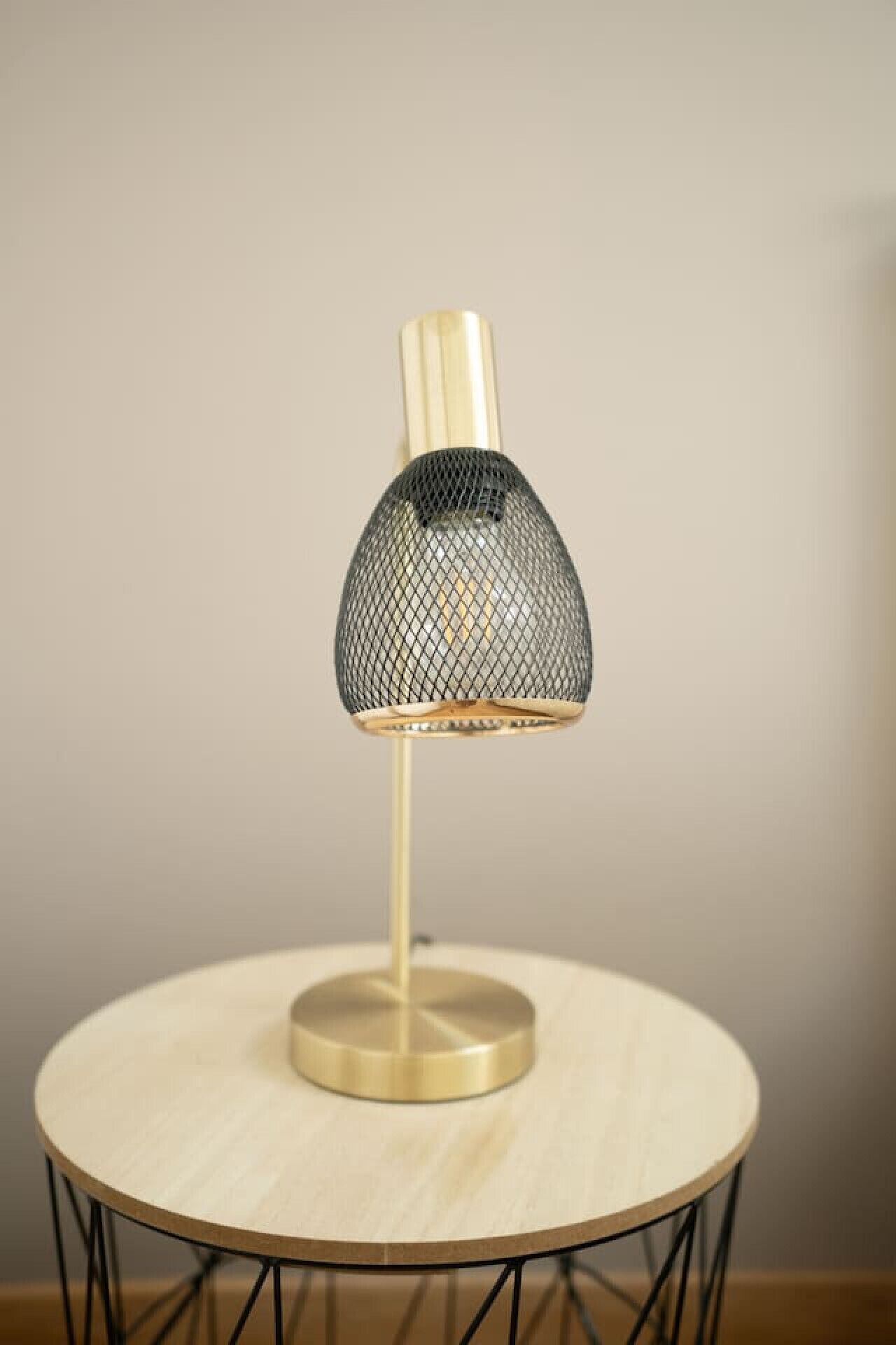 Een tafellamp met een metalen roosterlampenkap en houten voet op een rond tafel met een zwart metalen frame.