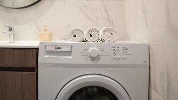 Een moderne wasruimte met een voorlader wasmachine, een houten kast, een spiegel en een betegelde muur van marmer.