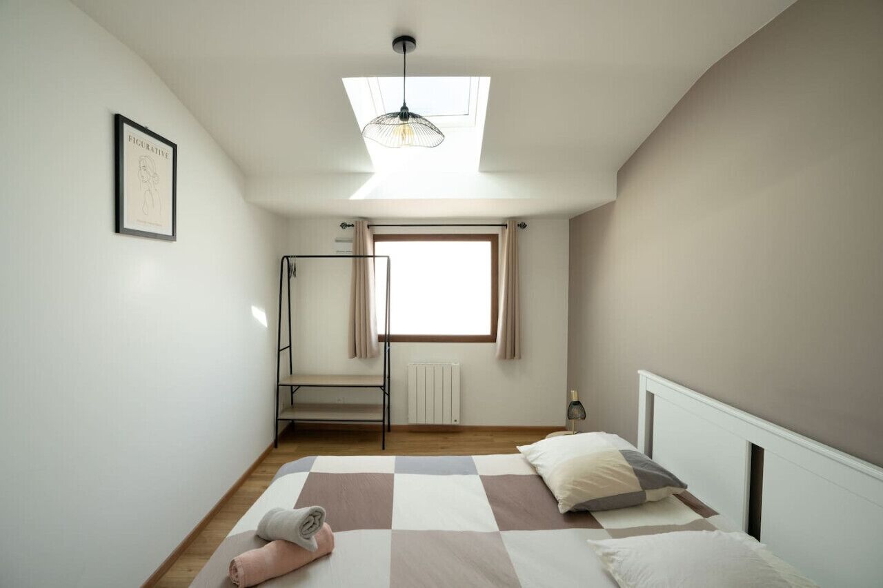 Ein Schlafzimmer mit Dachfenster, einem Bett mit kariertem Überwurf, einer Heizung und einem gerahmten Bild an der Wand.