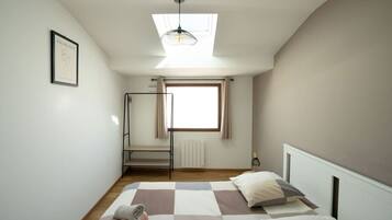 Ein Schlafzimmer mit Dachfenster, einem Bett mit kariertem Überwurf, einer Heizung und einem gerahmten Bild an der Wand.