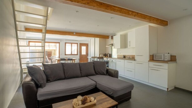 A modern living room with a sectional sofa, a wooden coffee table, and a kitchen area with white cabinets and a microwave.