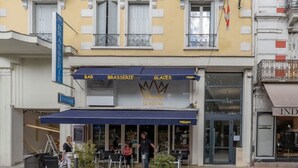 Ein Gebäude im klassischen Stil mit Balkonen und einer gelben Fassade, das im Erdgeschoss eine Bar und ein Restaurant beherbergt.