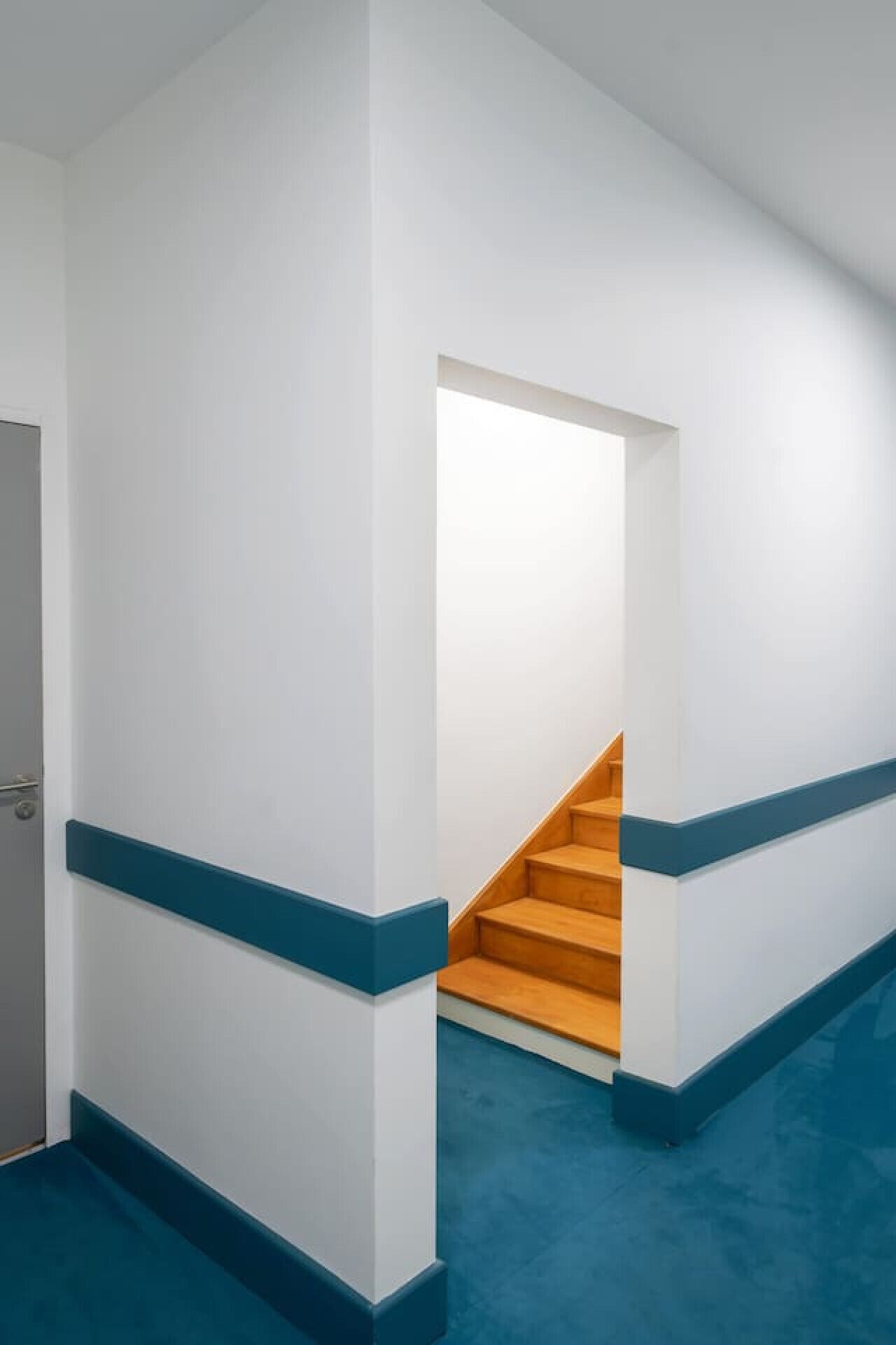 Un pasillo con paredes blancas y detalles azules que conduce a una escalera de madera.