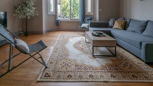 Ein geräumiges Wohnzimmer mit großem Fenster, einer Couch, einem Couchtisch und einem Sessel.