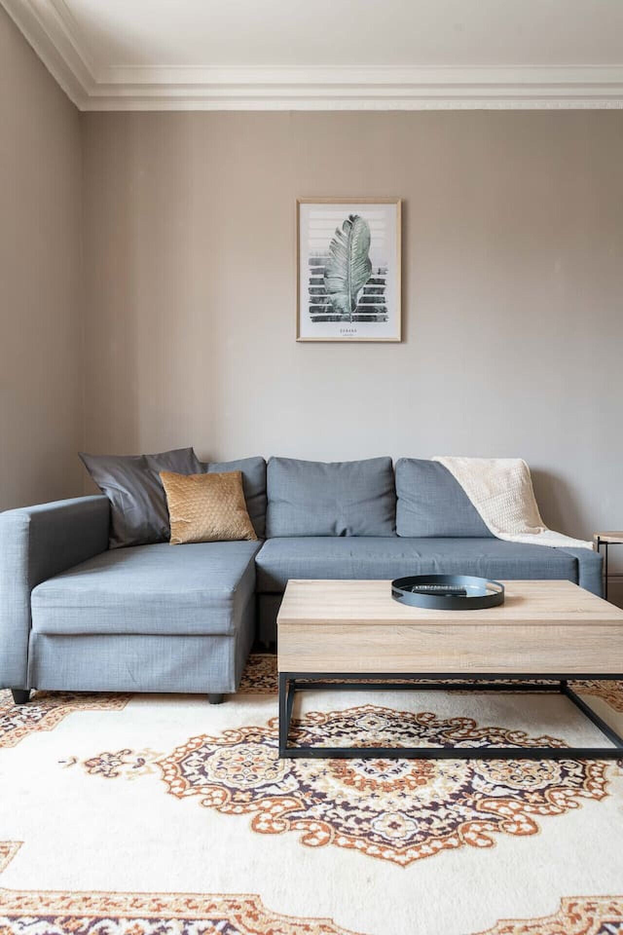 Un salon avec un canapé d’angle gris, une petite table basse et un tapis à motifs.