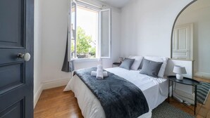Ein Schlafzimmer mit Bett, Nachttisch mit Lampe, Fenster mit Vorhängen und einer Tür.