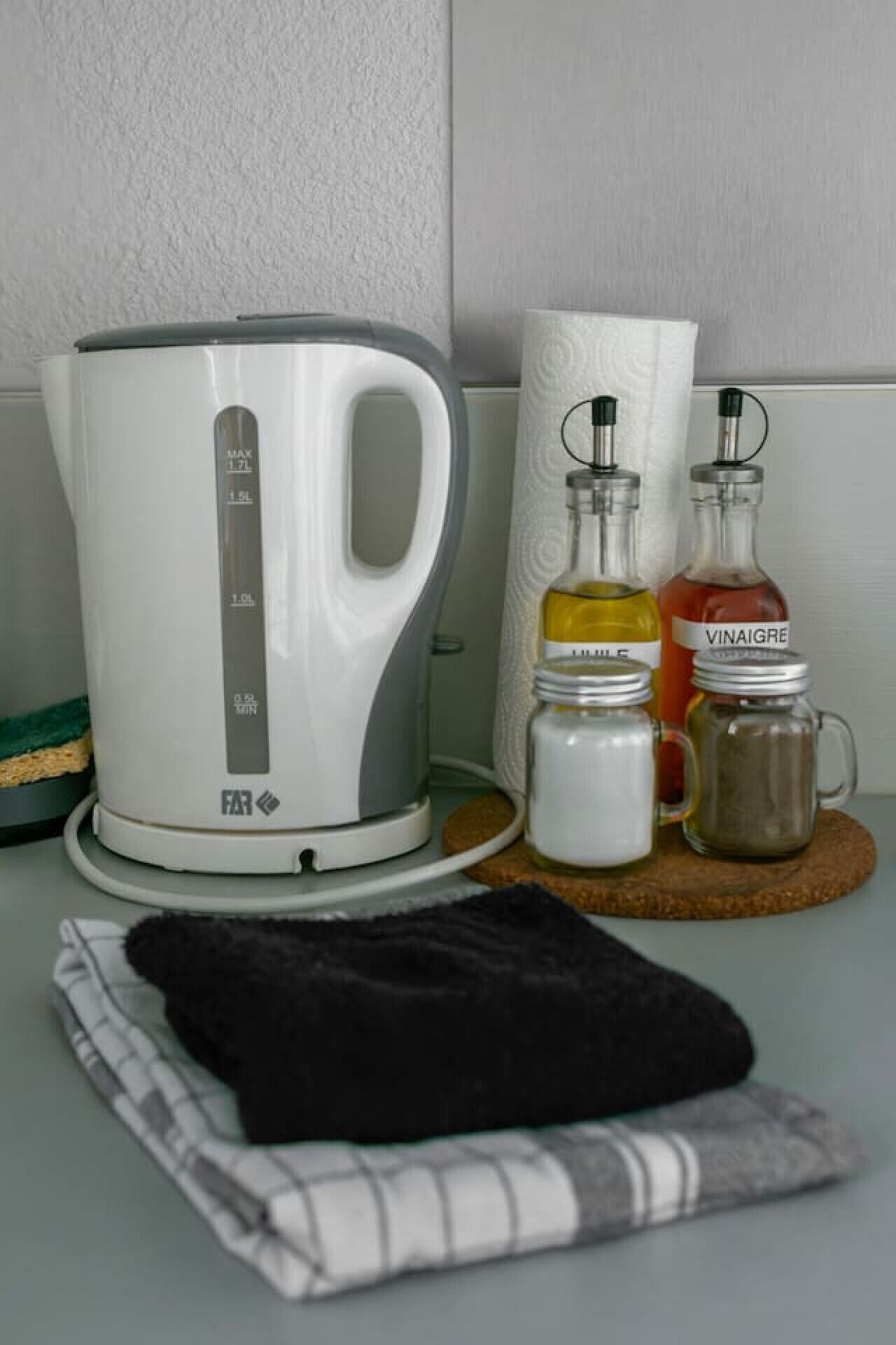 Une cuisine avec une bouilloire blanche, un porte-essuie-tout et des bocaux d’épices sur un plan de travail.