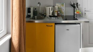 A compact kitchen with yellow cabinets, a black microwave, and a white refrigerator. - Appartement design Centre Ville proche Thermes (Vichy)
