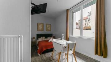 Una habitación con una cama, una mesa blanca con sillas, una ventana con cortinas y un radiador.